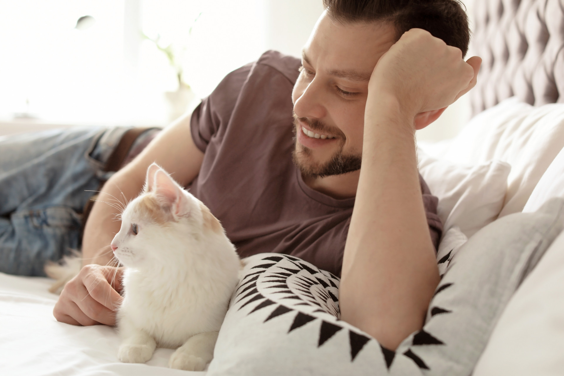 Young man with cute cat on bed at home