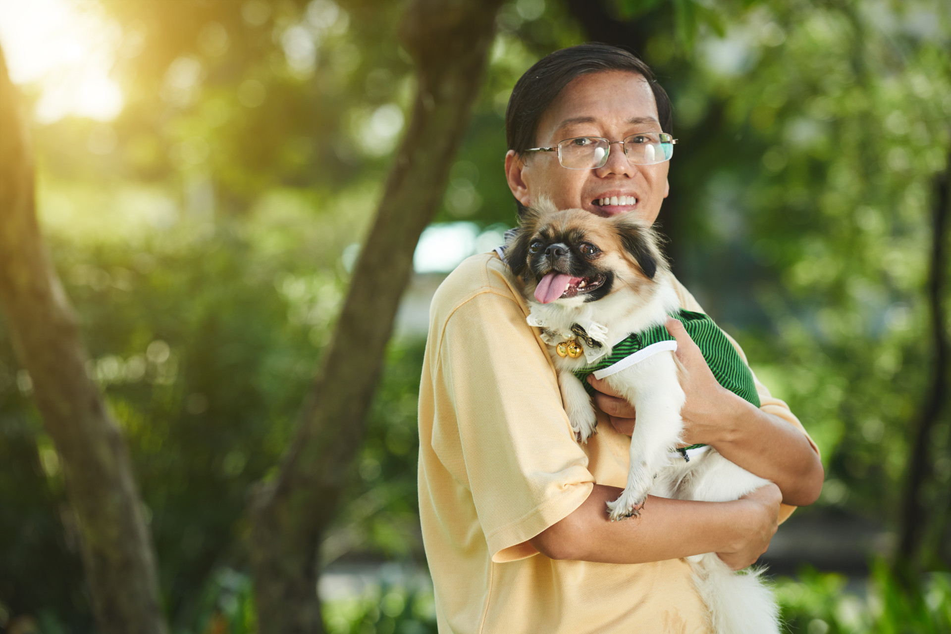 Cheerful Singaporean man standing with dog in his hands